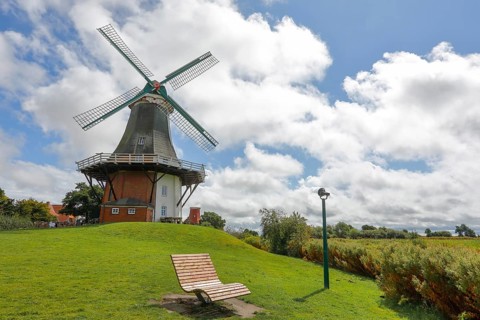 A windmill in front of a dramatic blue sky, surrounded by green meadows with a deckchair,