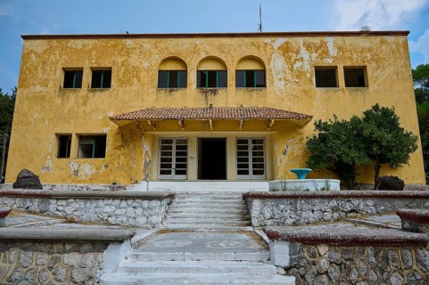 An old yellow dilapidated building with a damaged façade and a staircase in the entrance, Italian