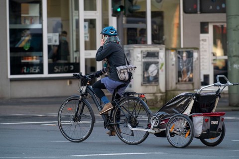 Woman riding a bicycle and child trailer, talking on mobile phone while riding, Bochum, North