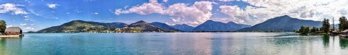Clear water of a lake with surrounding mountains, on a sunny day with blue sky and white clouds,