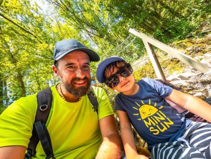 Father and son taking a selfie while hiking in a lush green forest, enjoying their summer vacation