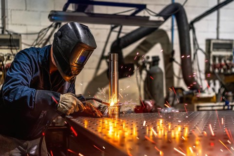 Unrecognizable male welder with protective facial mask and gloves welding a piece of metal in a