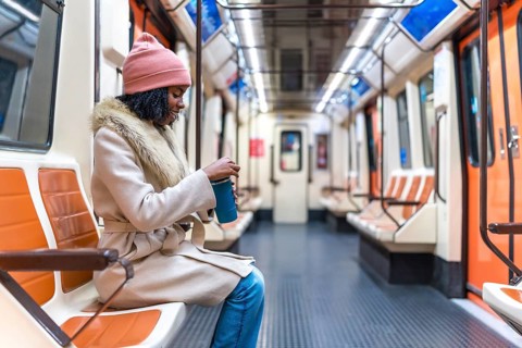 Passenger opening a reusable coffee cup while enjoying a quiet moment on a nearly empty subway