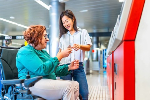 Chinese smiling caregiver buying metro ticket to a caucasian adult disabled woman in wheelchair