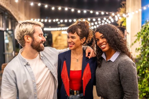 Happy friends embracing and smiling standing in a roof terrace at night celebrating party