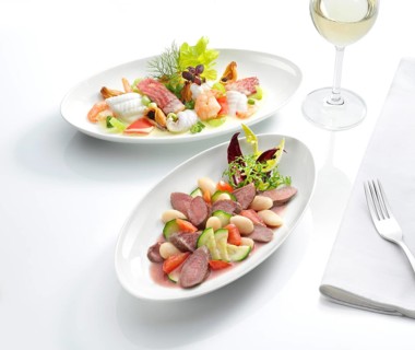 Two plates each with a meat dish and a fish dish, a glass with white wine, a fork on a napkin,