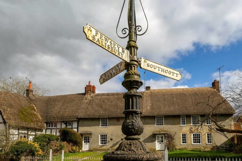 Historic signpost with direction painters, thatched cottages in village of Pewsey, Wiltshire,