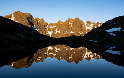 Rocky mountain peaks reflected in a small pond, mountain landscape with alpenglow at sunrise, at