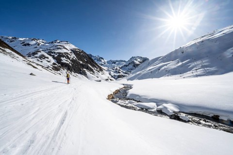 Ski tourer in the snow by a mountain stream in the Funtauna Valley, Sonnenstern, Graubünden Haute
