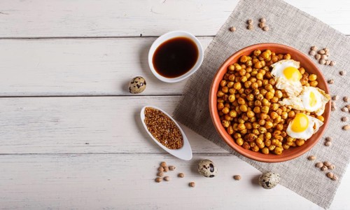 Fried chickpeas with quail eggs and spices in a clay plate on white wooden background, top view,
