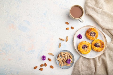 Small cheesecakes with jam and almonds with cup of coffee on a white concrete background and linen