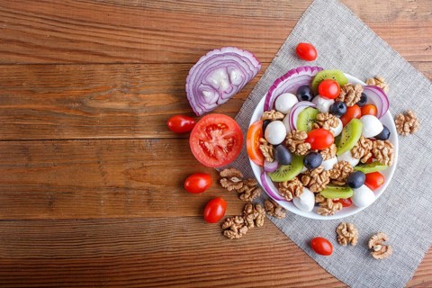 Salad with fresh cherry tomatoes, mozzarella cheese, olives, kiwi, onion and walnuts on brown