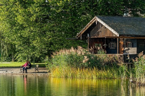 Wooden hut with common reed (Phragmites australis), two woman on a park bench, shore of Lake