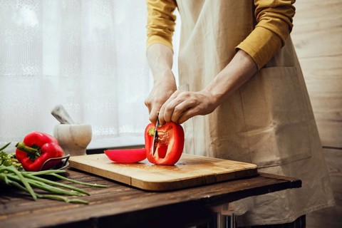 Unrecognizable man slicing red bell pepper with kitchen knife in the kitchen