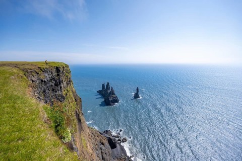Young man standing on cliff, view from steep cliff to the rocks Reynisdrangar in the water, at
