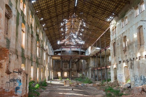 Abandoned industrial building with a large curved roof through which daylight falls, partially