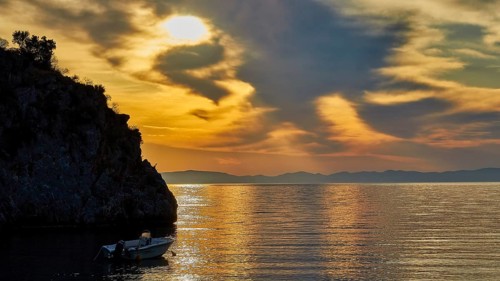 Atmospheric sunrise over the sea with cliffs and a boat, Mani Peninsula, Peloponnese, Greece,