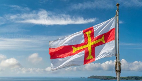The flag of the Isle of Guernsey, Great Britain, flutters in the wind