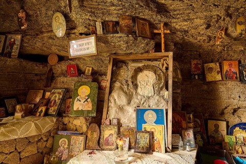 Altar area in a rock cave, surrounded by various crosses and religious symbols and icons, rock