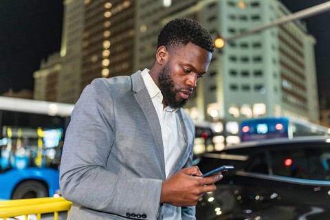 Young businessman using smartphone on city street at night, with blurred buildings and traffic in