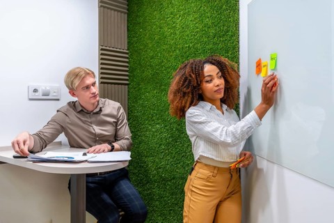 Businesswoman sticking notes on whiteboard while businessman analyzing reports in modern coworking