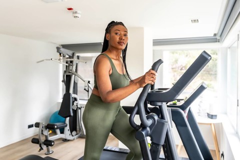 Businesswoman wearing olive green activewear using elliptical cross trainer in hotel fitness center