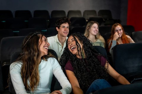 Friends enjoying laughter together while watching a comedy film at the cinema, sharing moments of