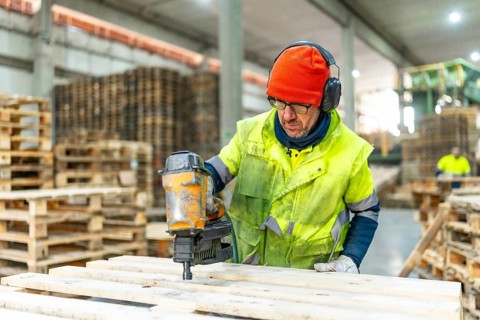 Man manual worker using compressed air gun to arrange pallets to reuse in a recycling plant