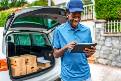African delivery man using digital tablet standing next to van with packages to deliver