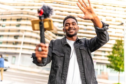 African man vlogger waving at camera while recording video blog in the city