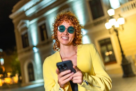 Cool modern woman in sunglasses using mobile phone standing in the city at night