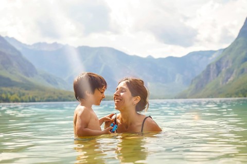 Mother and son enjoying summer holidays, playing in the refreshing water of lake bohinj, surrounded
