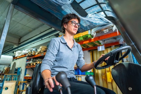 Concentrated cacuasian adult woman working with forklift in a warehouse of a metallurgic factory