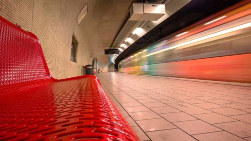 Modern underground railway track bed with red bench and passing train at high speed