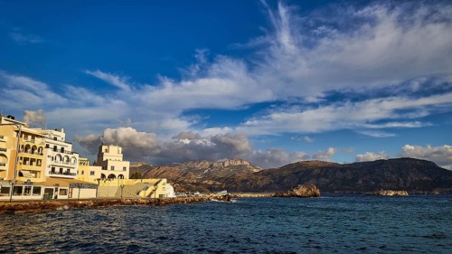 Morning light, coastal town with buildings by the sea and mountains in the background, Pigadia,