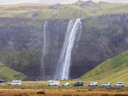 Tourist groups at waterfall Seljalandsfoss on a rainy day, queue at the path behind the waterfall,