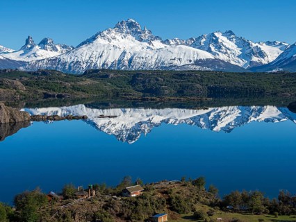 The snow-covered Mt. Cerro Castillo is reflected in a lake, small farm by the lake, Patagonia,