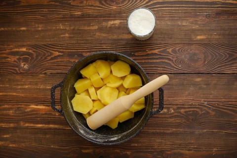 Top view of a kitchen table with boiled potatoes in a pot, potato masher and glass of warm milk