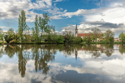 Huttenheim village reflected in a natural tree-lined river in spring. Bas Rhin, Alsace, France,