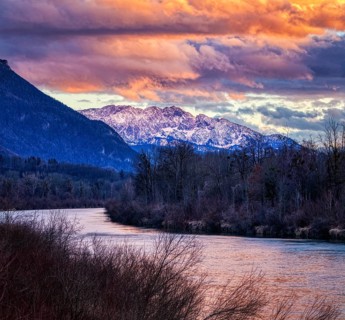 Mountain landscape at sunset with river, snow-covered peaks and dramatic cloudy sky, River Inn,