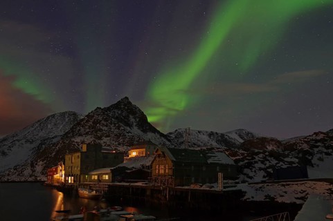 Night scene with northern lights in the sky, mountains in the background and illuminated houses on