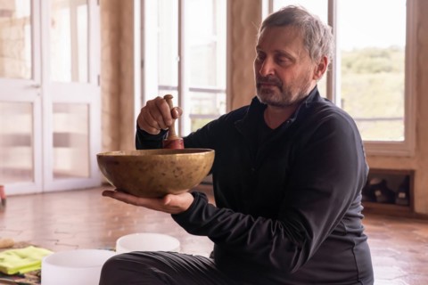 In a serene room, a mature man sits calmly, with a serene expression as he gently plays a bronze