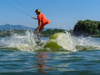 Young casual man with flapping shirt on wakeboard jumping into the lake, water ski and wakepark,