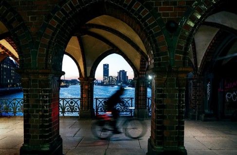 Bicycle rider to the sunrise at the Oberbaum Bridge, view through the arcades over the Spree to the