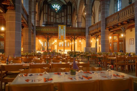 Several laid tables in a warmly lit church with organ in the background, Vesperkirche Calw, Black