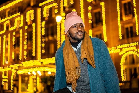 African man sitting outdoors during Christmas night facing Christmas fairy lights decorating a