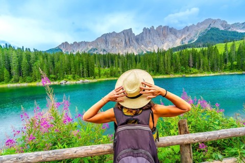 Female hiker with backpack holding her straw hat while admiring the turquoise waters of lake