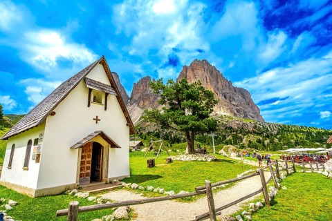 Tourists enjoying a sunny day at sella pass, with the chapel and the sassolungo group in the