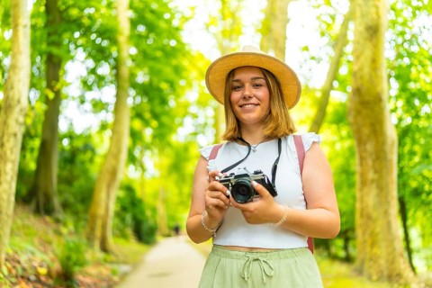 Portrait of a caucasian female young photographer standing in the forest smiling at camera and