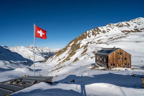 Swiss flag and mountain hut Keschhütte in front of mountain landscape in winter, behind summit of
